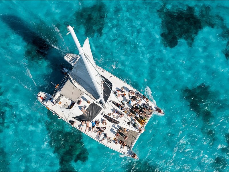 A catamaran at anchor over turquoise water and dark reef patches, seen from above