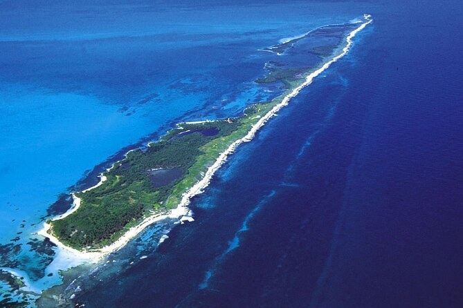 A long, narrow island seen from the air, surf breaking white along its reef edge