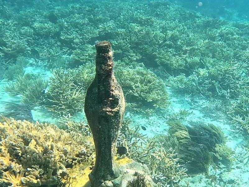 A single sculpture standing upright among branching coral on the sand