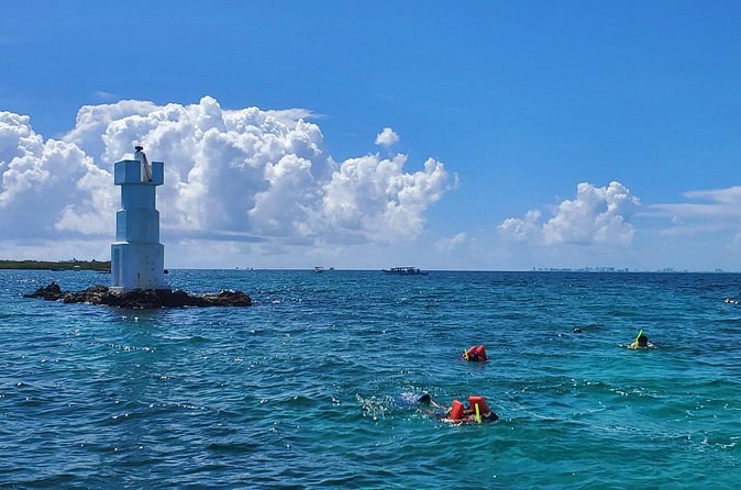 Snorkelers in life jackets in the channel beside a small lighthouse on a rock