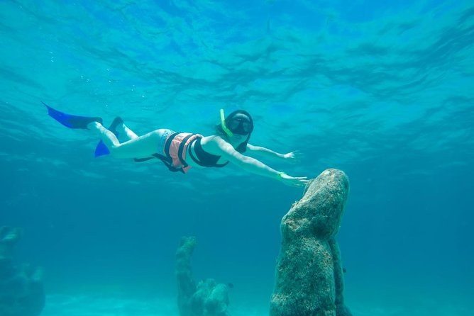 A snorkeler in fins diving down to touch the head of a statue